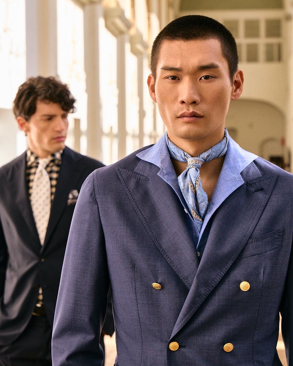 close-up of a confident-looking man wearing a light-blue kravat & shirt with a darker blue double-breasted suit